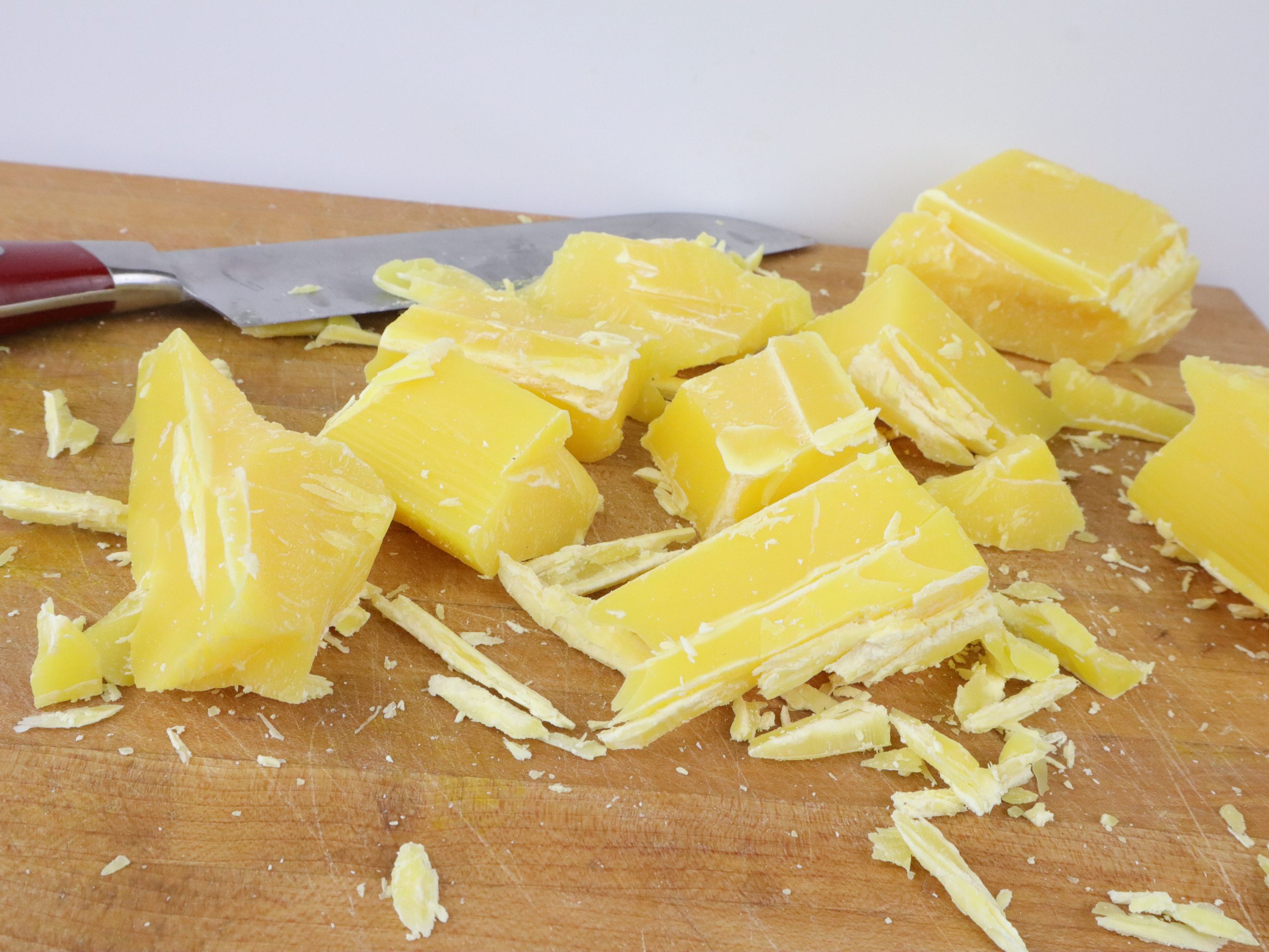 chunks of beeswax chopped up on a wooden cutting board with a knife