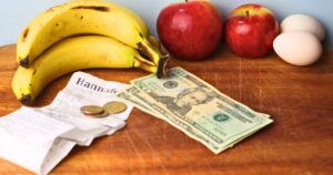 apples, bananas, eggs, a budget grocery receipt and cash on a wooden sideboard