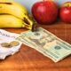 apples, bananas, eggs, a budget grocery receipt and cash on a wooden sideboard