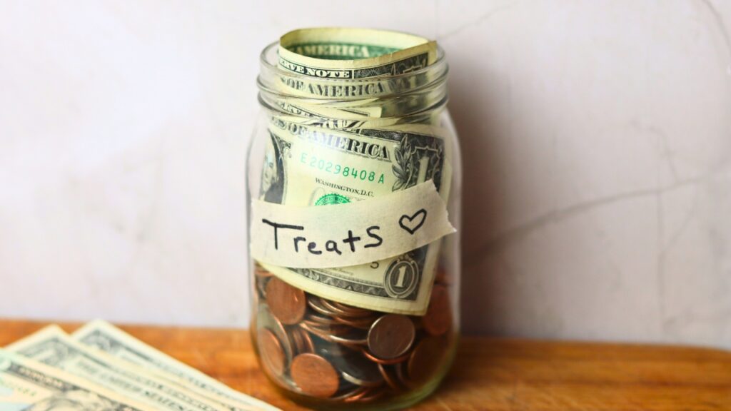 Glass jar full of loose change and dollar bills on wooden countertop.